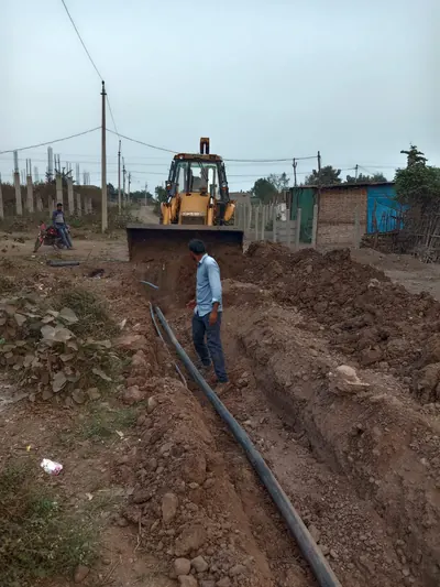 JCB digging a trench while an HDPE water main is laid