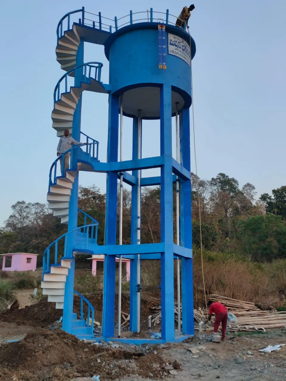 Blue RCC overhead tank with a spiral staircase, workers finishing it