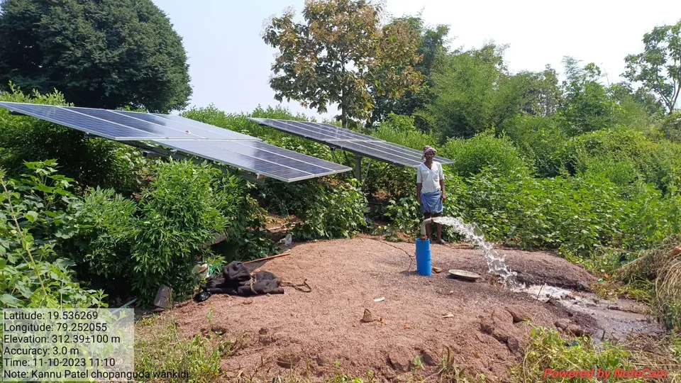 Solar panels powering a borewell pump, water gushing from the pipe on a farm