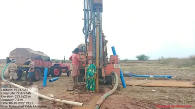 Orange rig drilling a borewell in a field, crew and farmer beside the drill pipe
