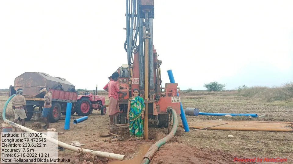 Drilling rig at work on a new borewell in a farm field, with the crew, a tractor and blue casing pipes