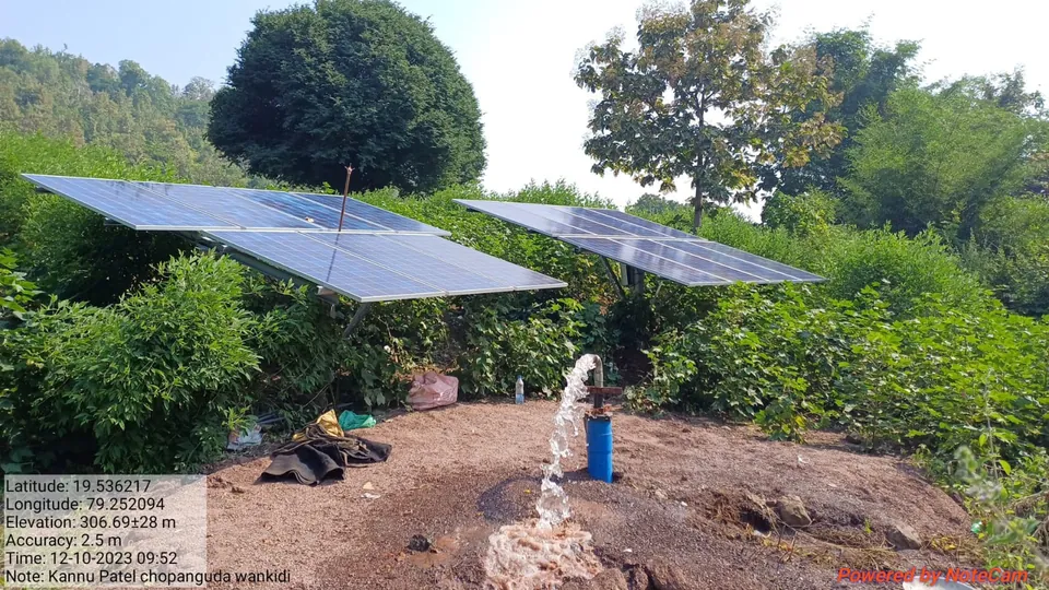 Two solar panel arrays on a farm powering a borewell pump, water gushing from the outlet